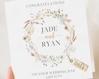 May include: A white wedding card with the words "Congratulations" at the top. The card features a floral wreath surrounding the names "Jade and Ryan" in black and gold. A tag with "2024" hangs from the wreath. The text "On Your Wedding Day 23rd June" is at the bottom.