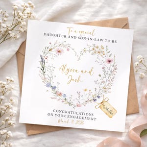 Op de afbeelding: Een vierkante verlovingskaart met een bloemenhartontwerp. De kaart bevat de gouden tekst "Aan een speciale dochter en schoonzoon", met de namen "Alyssa en Josh". De tekst "Gefeliciteerd met jullie verloving 11 maart 2026" is ook aanwezig.