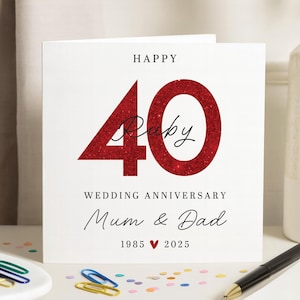 May include: A white card with the words "HAPPY" at the top. The number "40" is in red glitter, with "Ruby" written in cursive. Below, it reads "WEDDING ANNIVERSARY Mum & Dad 1985 ❤️ 2025".