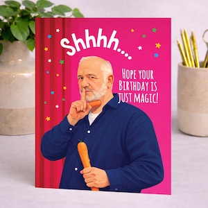 May include: A birthday card with a pink background featuring an illustration of a man holding a carrot and shushing. The card reads "Shhhh... HOPE YOUR BIRTHDAY IS JUST MAGIC!" with star accents.