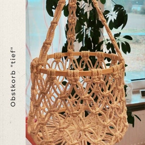 May include: A white macrame hanging basket with a wooden rim. The basket is hanging from a white rope and has a knotted design.