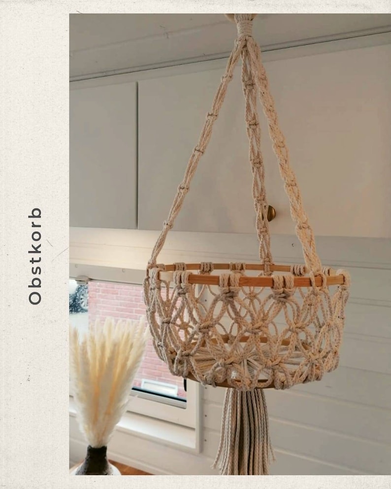 Puede incluir: Una cesta de fruta de macram&eacute; colgante con una base de madera natural y un borla de color crema. La cesta est&aacute; colgada de un techo blanco.