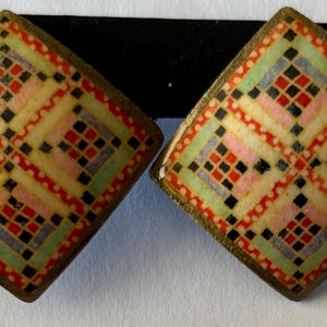 May include: Pair of square earrings with a colorful geometric pattern. The earrings feature a gold-toned border and a design with red, black, pink, green, and yellow squares. The earrings are displayed on a black backing.
