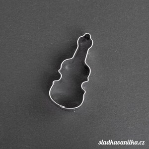 Pode incluir: Um cortador de biscoitos de metal prateado em forma de violino. O cortador está sobre um fundo cinza escuro.