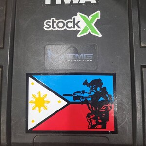 May include: A black hard case with a sticker of the Philippine flag and a soldier holding a rifle. The case also has stickers for KWA, stockX, and EMG International.