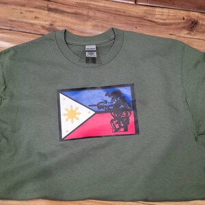 May include: A green t-shirt with a graphic of a soldier holding a rifle in front of the Philippine flag.