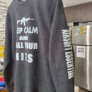 May include: A dark gray sweatshirt with a white graphic print that says "Keep Calm and Call Your Hits" and a white graphic print on the sleeve that says "Airsoft Essential".