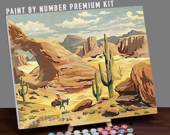 Peut inclure: Kit de peinture par numéros représentant un paysage désertique avec une arche rocheuse naturelle, des cactus et un cavalier solitaire à cheval. Le kit comprend une toile, des peintures et des pinceaux.