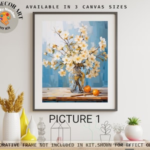 Könnte beinhalten: Ein gerahmtes Paint-by-Number-DIY-Kit mit einem Stillleben aus weißen Blumen in einer Glasvase, mit Orangen und einem Zimtstiel auf einer Holzoberfläche. Der Hintergrund ist blau. Der Text auf dem Bild lautet "AVAILABLE IN 3 CANVAS SIZES" und "PICTURE 1".