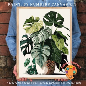 Peut inclure: Un kit de peinture par num&eacute;ros encadr&eacute; repr&eacute;sentant une illustration de plante Monstera. L'&oelig;uvre pr&eacute;sente de grandes feuilles vertes aux motifs distinctifs, sur fond neutre. Le texte "PAINT. BY NUMBERS CANVAS KIT" est en haut.