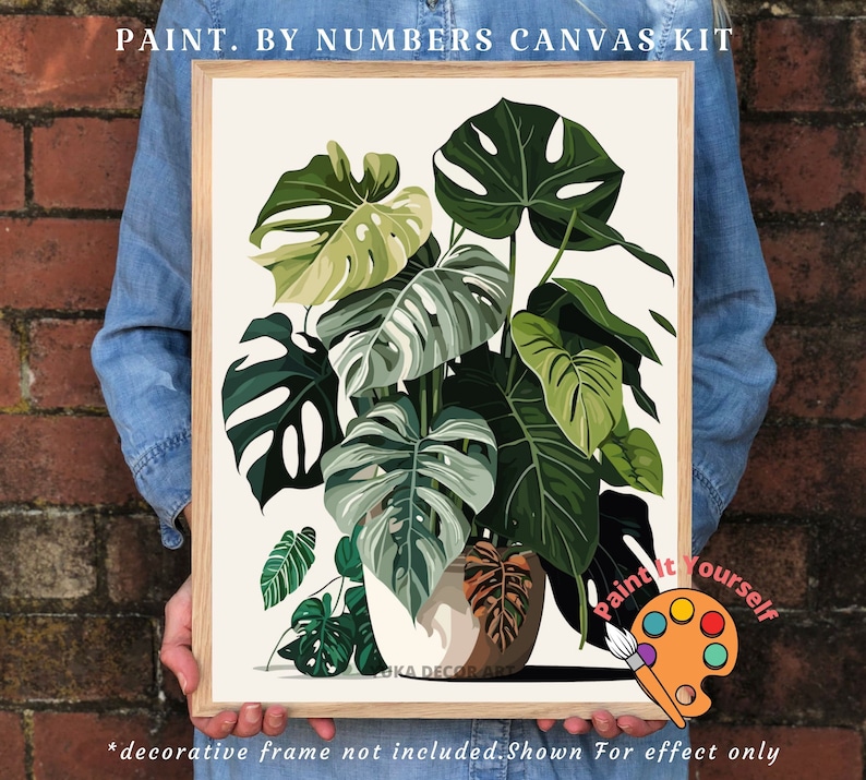 Peut inclure: Un kit de peinture par num&eacute;ros encadr&eacute; repr&eacute;sentant une illustration de plante Monstera. L'&oelig;uvre pr&eacute;sente de grandes feuilles vertes aux motifs distinctifs, sur fond neutre. Le texte "PAINT. BY NUMBERS CANVAS KIT" est en haut.