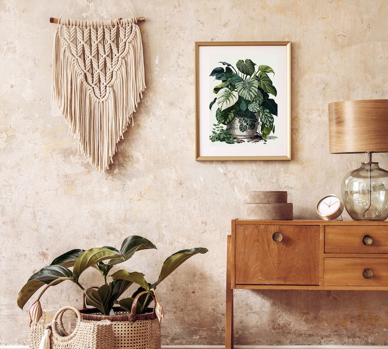 Op de afbeelding: Een botanische print in een gouden lijst toont weelderige groene planten in een decoratieve pot, opgehangen aan een getextureerde muur. Een macram&eacute; wandkleed en een houten bijzettafel met een lamp en klok maken de inrichting compleet. Een grote potplant in een geweven mand staat op de vloer.