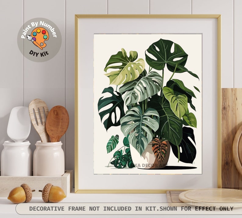 Peut inclure: Une impression encadr&eacute;e d'une plante Monstera avec de grandes feuilles vertes, dans un cadre dor&eacute;. L'image fait partie d'un kit de peinture par num&eacute;ros &agrave; faire soi-m&ecirc;me. Le texte en bas indique : "CADRE D&Eacute;CORATIF NON INCLUS DANS LE KIT. MONTRE &Agrave; TITRE D'EFFET UNIQUEMENT."