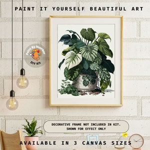 Op de afbeelding: Een ingelijste paint-by-number kit met een botanische illustratie van groene en witte planten in een decoratieve pot. Het kunstwerk wordt op een witte achtergrond weergegeven, met de tekst "PAINT IT YOURSELF BEAUTIFUL ART". Verkrijgbaar in 3 canvasmaten.