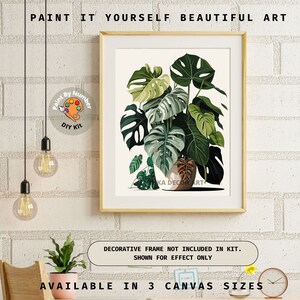 Peut inclure: Un kit de bricolage de peinture par num&eacute;ros encadr&eacute;, repr&eacute;sentant une illustration botanique d'une plante Monstera avec de grandes feuilles vertes. L'&oelig;uvre est dans un cadre clair. Le texte en haut indique "PAINT IT YOURSELF BEAUTIFUL ART."