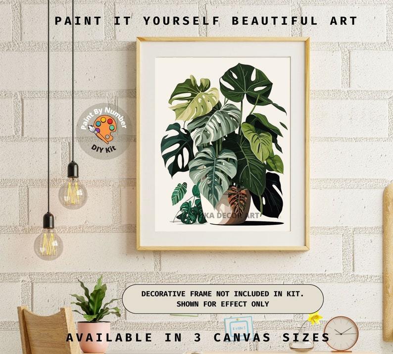 Peut inclure: Un kit de bricolage de peinture par num&eacute;ros encadr&eacute;, repr&eacute;sentant une illustration botanique d'une plante Monstera avec de grandes feuilles vertes. L'&oelig;uvre est dans un cadre clair. Le texte en haut indique "PAINT IT YOURSELF BEAUTIFUL ART."