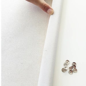 Peut inclure: Une toile blanche avec un bord pli&eacute;, montrant le tissu brut. Un groupe de punaises argent&eacute;es sont dispers&eacute;es sur une surface blanche.