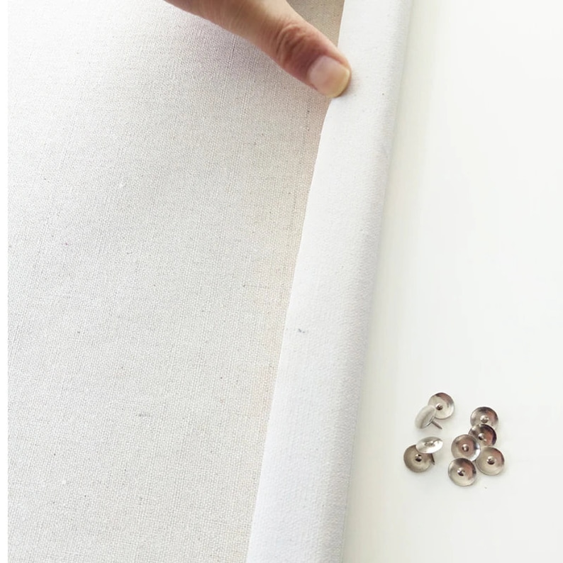 Peut inclure: Une toile blanche avec un bord pli&eacute;, montrant le tissu brut. Un groupe de punaises argent&eacute;es sont dispers&eacute;es sur une surface blanche.