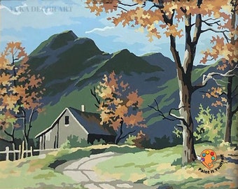 May include: A paint by numbers kit featuring a landscape scene with a small house, trees, and mountains in the background. The scene is painted in a stylized, cartoonish style with bright colors. The kit includes a canvas, paints, and brushes. "Paint it yourself" is written on the bottom right corner of the image.