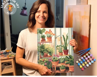 May include: A woman holds a paint by number kit featuring a colorful illustration of a room filled with potted plants. The kit includes a canvas, paintbrushes, and numbered paint pots. The text on the canvas reads "Express Yourself Through Art".