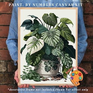 Op de afbeelding: Een paint-by-numbers canvas kit met een gedetailleerde illustratie van weelderige groene planten in een witte pot. Het kunstwerk bevat verschillende tinten groen en wit, met de tekst "PAINT. BY NUMBERS CANVAS KIT" bovenaan. De tekst "Paint it Yourself" is ook zichtbaar.