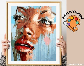 Puede incluir: Kit de pintura por números con un retrato de primer plano de la cara de una mujer con un fondo abstracto colorido. La mujer tiene piel morena, labios rojos y ojos azules. El texto "Paint It Yourself" es visible en la esquina superior derecha de la imagen.