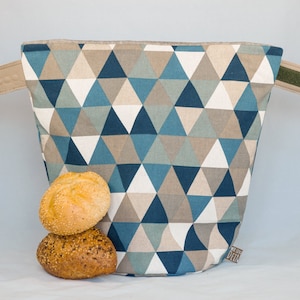 May include: A blue and brown geometric patterned fabric bread bag with two fabric handles. The bag is filled with two round bread rolls.