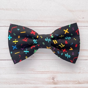May include: Black bow tie with a colorful math symbols pattern. The symbols include numbers, plus, minus, division, multiplication, percent, and pi.