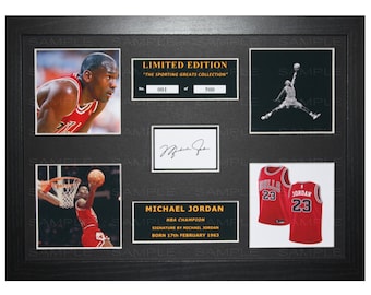 May include: A framed Michael Jordan memorabilia set with a black background. The set includes a photo of Jordan, a signature, a photo of Jordan in action, and a red Chicago Bulls jersey with the number 23. The text on the frame reads "Limited Edition - The Sporting Greats Collection - No. 001 of 500".
