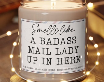 May include: A brown soy wax candle with a white label that reads "Smells like a badass mail lady up in here". The candle is 9 oz and has a burn time of 50-60 hours.