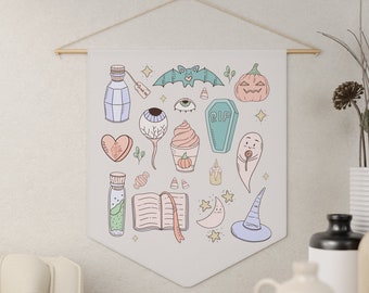 May include: A white canvas wall hanging with a variety of Halloween-themed illustrations, including a bat, a pumpkin, a ghost, a witch's hat, an eye, a coffin, a heart, a potion bottle, a book, a crescent moon, and a candy cane.