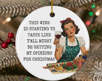 Peut inclure: Ornement de Noël rond et blanc avec une ficelle dorée. Il présente une illustration rétro d'une femme tenant un verre de vin rouge. Le texte sur l'ornement dit : "THIS WINE IS STARTING TO TASTE LIKE Y'ALL MIGHT BE GETTING MY OPINIONS FOR CHRISTMAS."