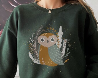 May include: A dark green sweatshirt with a graphic print of an owl surrounded by foliage. The owl is brown and gray with large eyes. The foliage is in shades of green, brown, and white.