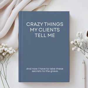 May include: A blue journal with the text "CRAZY THINGS MY CLIENTS TELL ME" in white. Below the title is the text "And now I have to take these secrets to the grave." The journal is on a white surface with flowers and a pen.