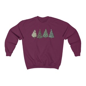 Peut inclure: Un sweat-shirt bordeaux avec une rang&eacute;e de quatre sapins de No&euml;l. Les arbres sont d&eacute;cor&eacute;s de divers ornements et lumi&egrave;res. Les arbres sont dans des tons de vert, blanc et or.