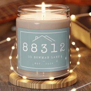 May include: A brown candle in a clear glass jar with a blue label. The label has a house icon, the number 88312, the text "111 Bowman Lane", and "EST. 2024".