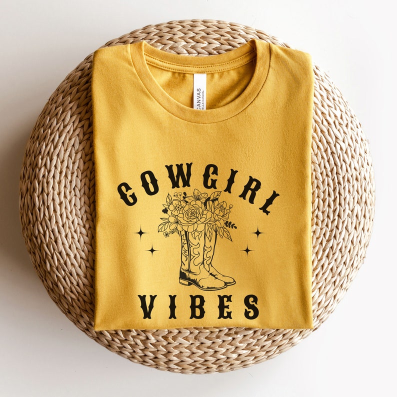May include: A mustard yellow t-shirt with a black graphic of cowboy boots with flowers and the text "COWGIRL VIBES".