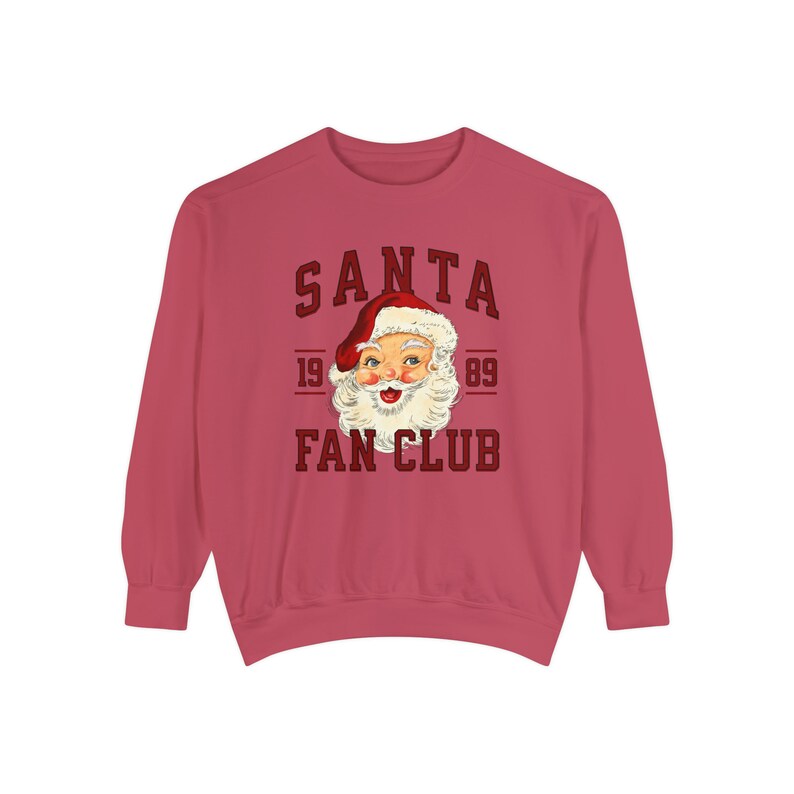 May include: A red long-sleeved sweatshirt with the text "SANTA FAN CLUB" in a red and white vintage style font. The text is surrounded by a red circle with the numbers "19 89" on either side. A cartoon image of Santa Claus's face is inside the circle.