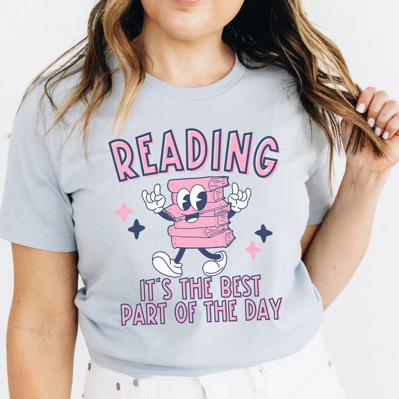 May include: A light blue t-shirt with a pink cartoon stack of books with a smiling face and the text "READING IT'S THE BEST PART OF THE DAY".