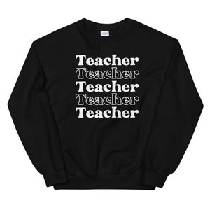 Puede incluir: Sudadera negra con la palabra "Teacher" repetida cinco veces en blanco, apilada verticalmente.