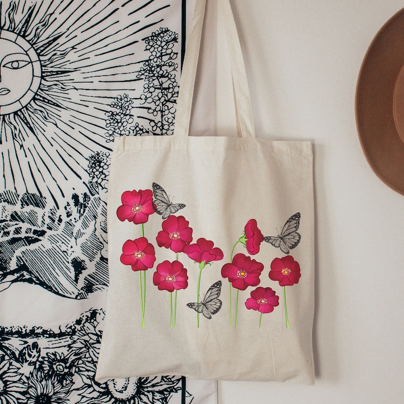 May include: A white canvas tote bag with a design of pink flowers and black butterflies. The bag has long straps.