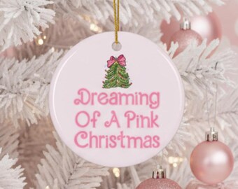 Puede incluir: Adorno navideño redondo y blanco con el texto rosa "Dreaming Of A Pink Christmas". El adorno presenta un árbol de Navidad verde con un lazo rosa. Se adjunta un hilo dorado para colgarlo.