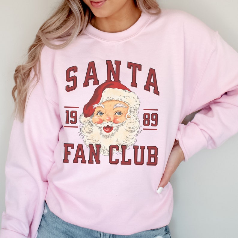 May include: Pink sweatshirt with a vintage Santa Claus graphic and the text "SANTA FAN CLUB 19 89".