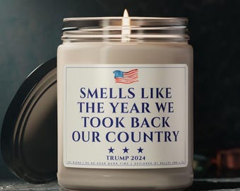 May include: A beige candle jar with a white label that reads "Smells Like The Year We Took Back Our Country" with a small American flag and the text "Trump 2024" below.