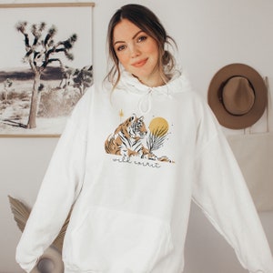 May include: White hooded sweatshirt with a graphic of a tiger, a sun, and a star. The text "wild spirit" is printed below the tiger.