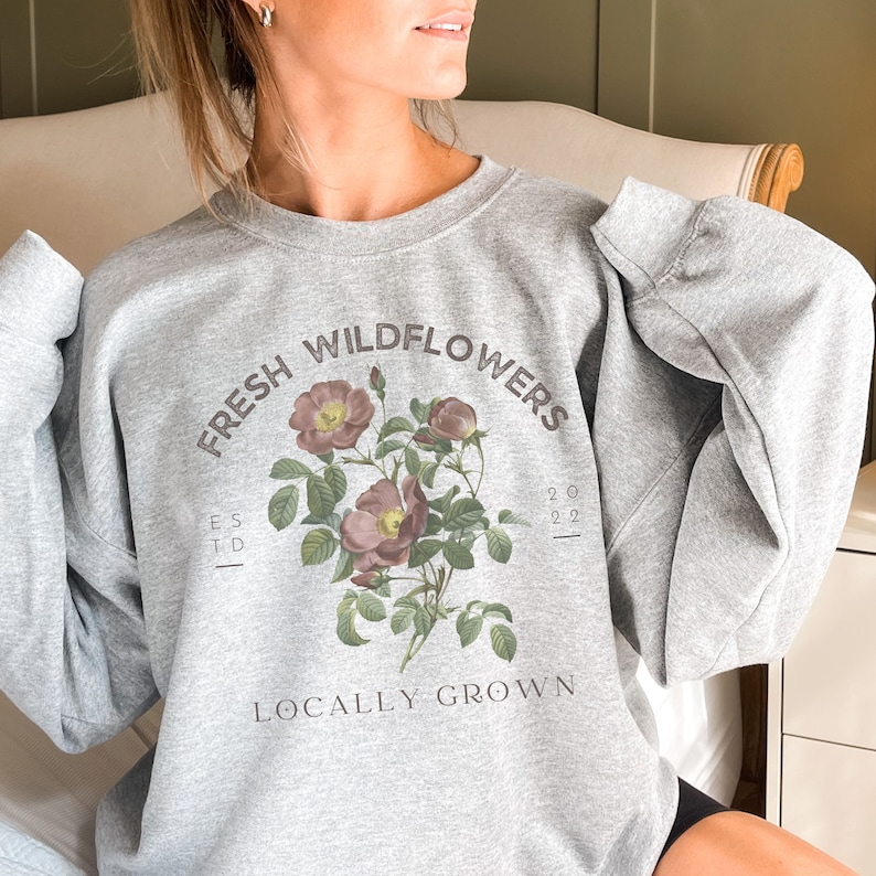 May include: Gray sweatshirt with a floral design and the text "Fresh Wildflowers Est. 2022 Locally Grown".