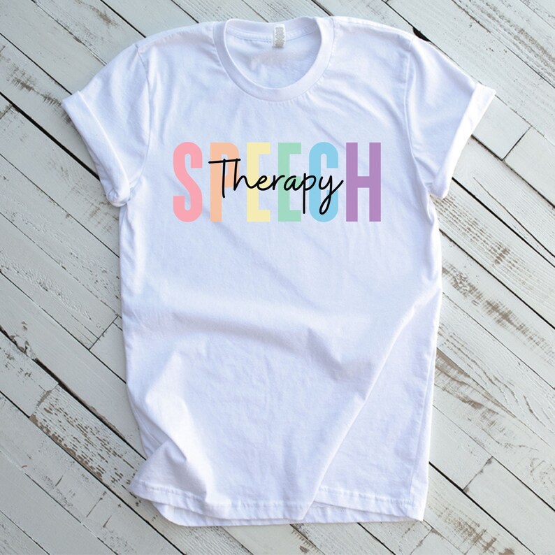 Puede incluir: Camiseta blanca con el texto "Speech Therapy" en colores arco&iacute;ris.