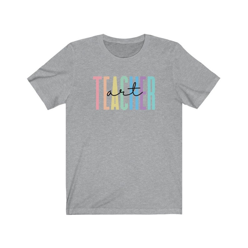May include: A heather gray t-shirt with the word "TEACHER" in vertical pastel colors and the word "art" in cursive. The shirt is made of a soft material and has a crew neck.