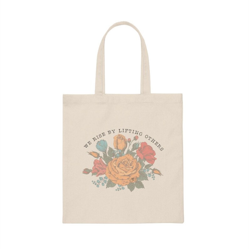 May include: A beige tote bag with a floral design and the text "We rise by lifting others".