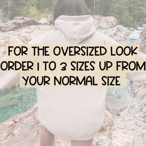 May include: A person wearing a light beige oversized hoodie with the text "FOR THE OVERSIZED LOOK ORDER 1 TO 3 SIZES UP FROM YOUR NORMAL SIZE" printed on the front.